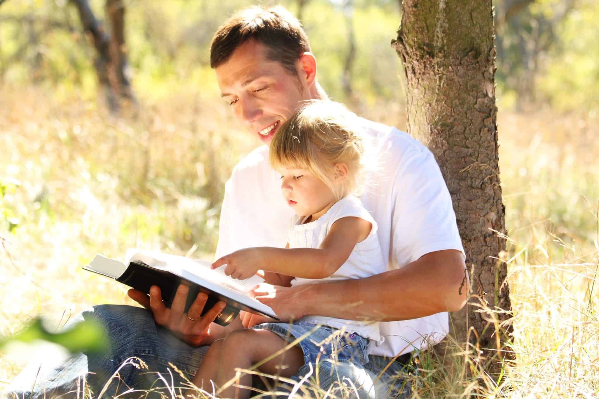 Father and daughter reading Bible in the park