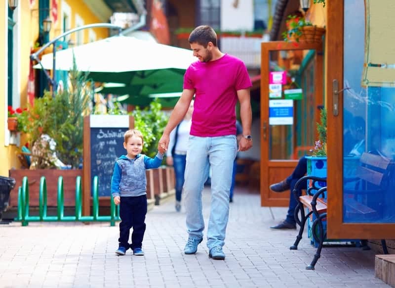 Father and son holding hands walking downtown in small town