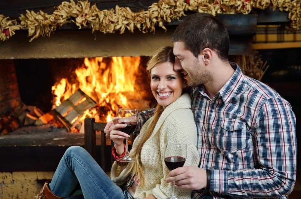 Happy couple drinking wine by the fireplace in a cabin rental in Murphy NC