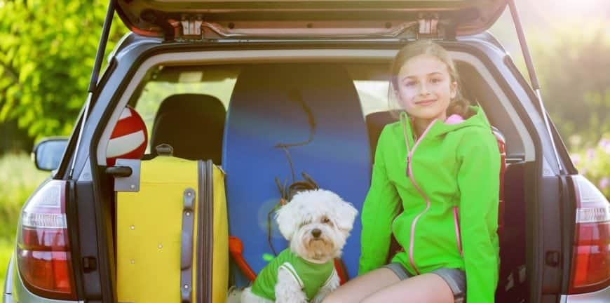 Little girl with her dog packed for vacation in the car