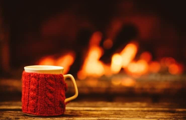 A mug with a wool koozie on a table in front of the fireplace.