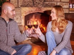 A couple drinking wine in front of their cabin's fireplace.