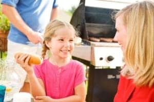 A young girl holding a hot dog while talking to her mother outdoors.