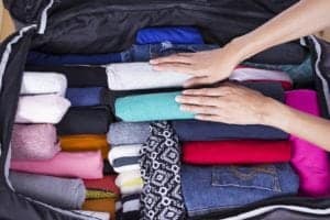 A woman packing rolled clothes in a suitcase.