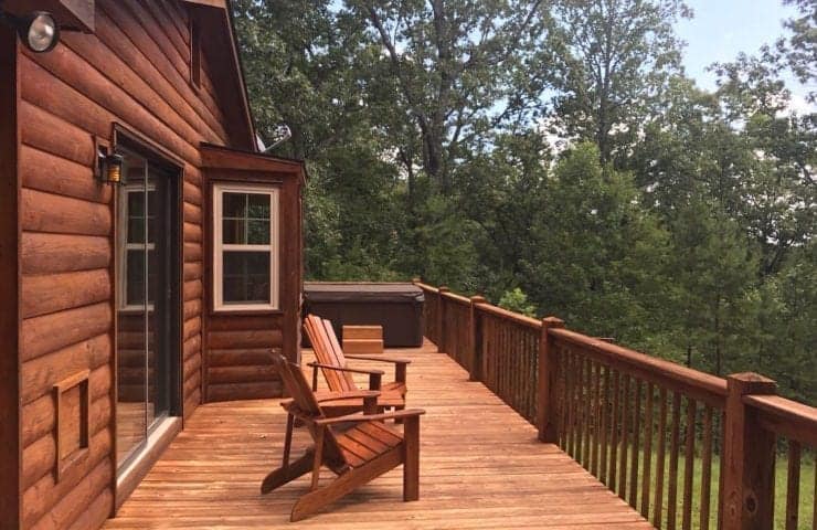 back deck of a cabin with chairs surrounded by woods