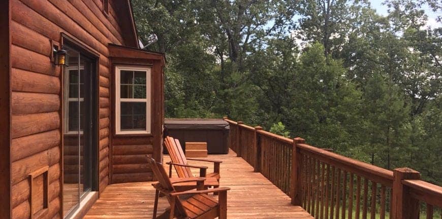 back deck of a cabin with chairs surrounded by woods
